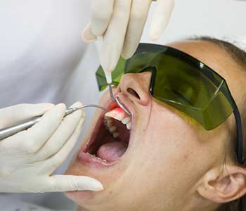 Dentist using a modern diode dental laser for periodontal care. Patient wearing protective glasses, preventing eyesight damage.
